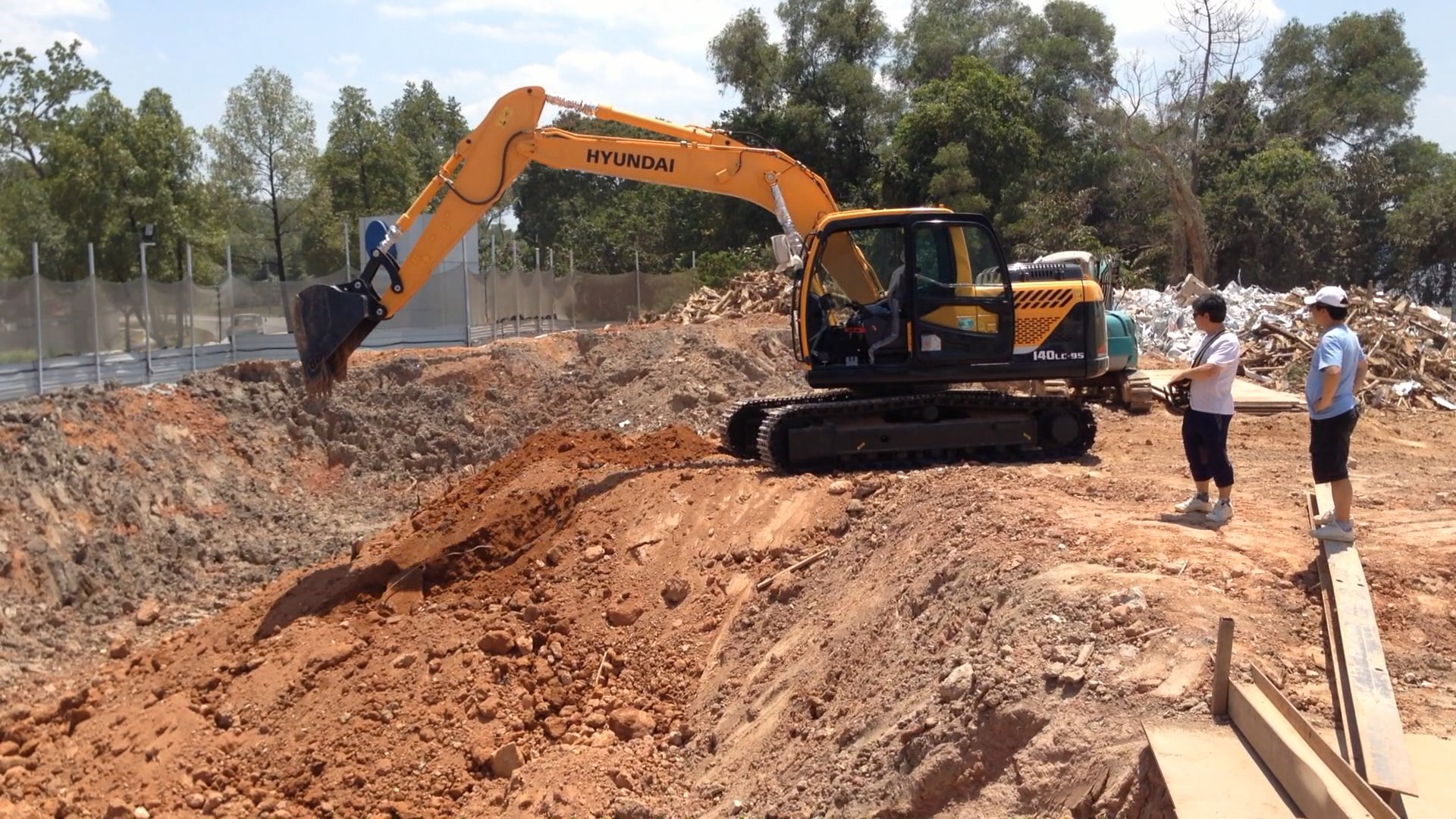 Operator beside an excavator using a remote controller at a work site